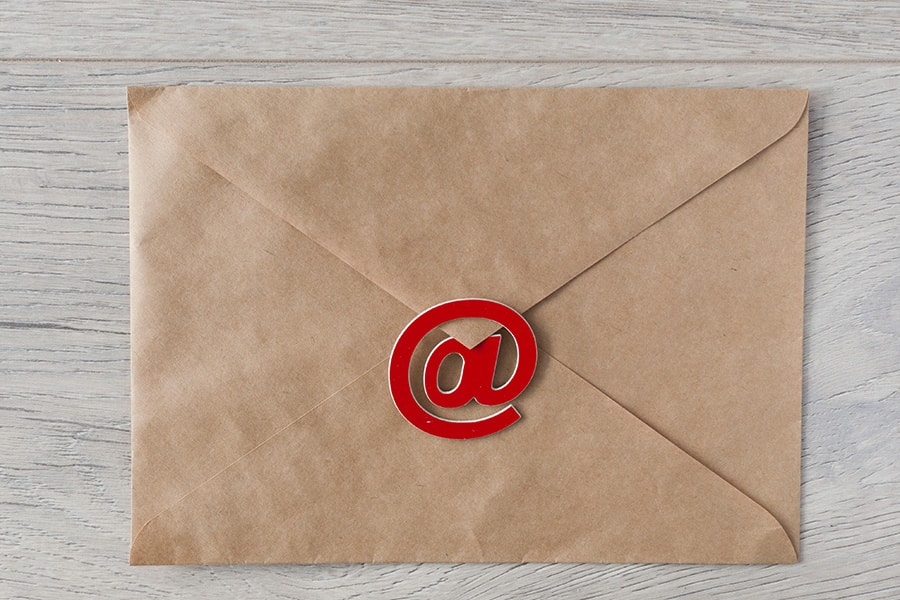 #84 liste email - enveloppe en papier kraft avec un "@" rouge sur un fond bois blanc