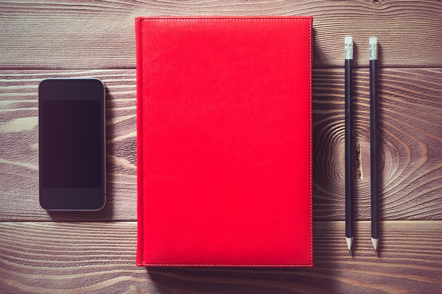 Illustration pour article légendes Instagram : smartphone, carnet rouge et crayons noirs posés sur un bureau en bois