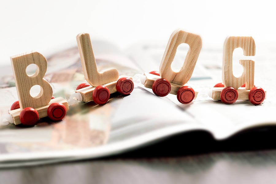 #91 blog d'entreprise - le mot BLOG en lettre de bois sur roulettes posé sur un magazine ouvert